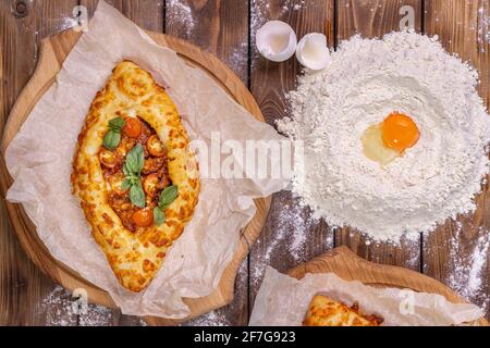 Khachapuri liegt auf hölzernen runden Pizzabrettern und Hühnereiern auf einem braunen Bretthintergrund. Flaches Layout. Stockfoto
