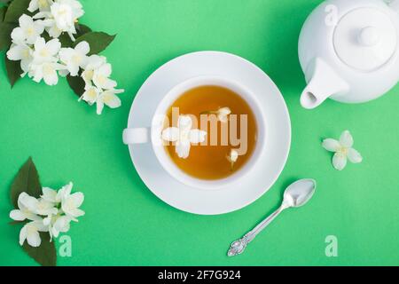 Grüner Jasmintee in der weißen Tasse, Teekannen und Blumen auf grünem Hintergrund. Draufsicht. Nahaufnahme. Stockfoto