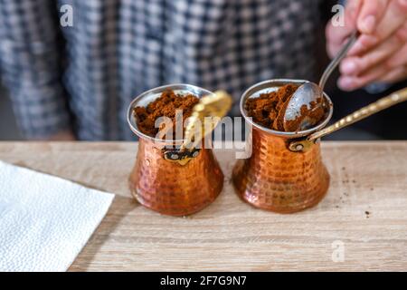 Der Barista legt natürlichen gemahlenen Kaffee in die Kupferbecher. Der Prozess der Herstellung eines Getränks. Stockfoto