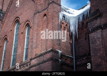 Eiszapfen hängen an einem Wintertag im Februar 2021 an der Seite einer alten Kirche in London, Ontario, Kanada, inmitten von COVID-19 Pandemiesperrungen. Stockfoto