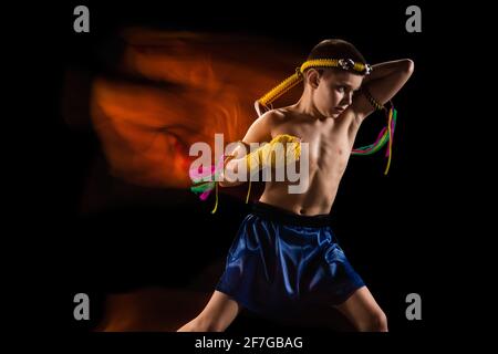 Kleiner Junge trainiert thai Boxen auf schwarzem Hintergrund. Kämpfer üben, Training in der Kampfkunst in Aktion, Bewegung. Evolution der Bewegung, Fang Stockfoto
