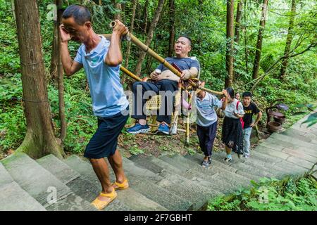 ZHANGJIAJIE, CHINA - 9. AUGUST 2018: Träger einer Limousine Stuhl mit einem Besucher des Zhangjiajie National Forest Park in der Provinz Hunan, China Stockfoto