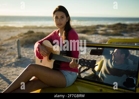 Kaukasische Frau, die auf dem Strandbuggy sitzt und Gitarre spielt, Mann, der hinter dem Lenkrad sitzt Stockfoto