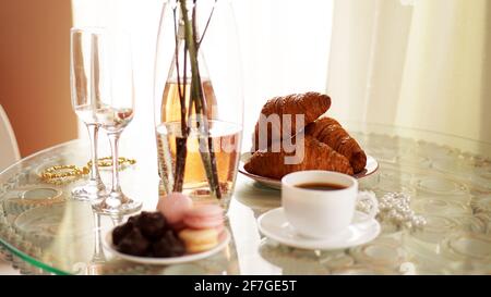 Glastisch mit einer Tasse Kaffee, süßen Croissants. Flasche Wein und Gläser Stockfoto