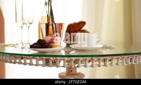 Glastisch mit einer Tasse Kaffee, süßen Croissants. Flasche Wein und Gläser Stockfoto