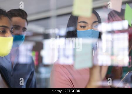 Eine vielfältige Gruppe kreativer Kollegen trägt Masken beim Brainstorming mit Glas Wand Stockfoto