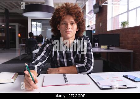 Porträt eines Geschäftsmannes mit gemischter Rasse im Büro, das in der Hand sitzt Bleistift mit Blick auf die Kamera Stockfoto