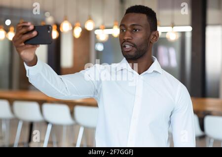 Zwangloser afroamerikanischer Geschäftsmann, der Selfie nimmt und Smartphone benutzt Stockfoto