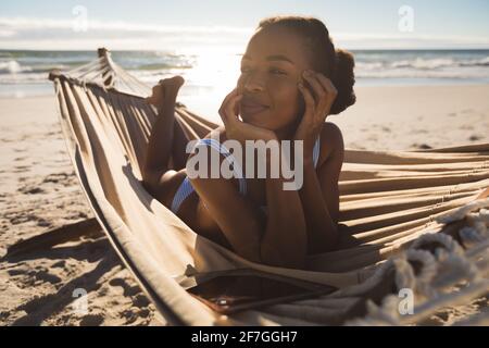 Glückliche afroamerikanische Frau, die in der Hängematte am Strand liegt und sucht Voraus Stockfoto