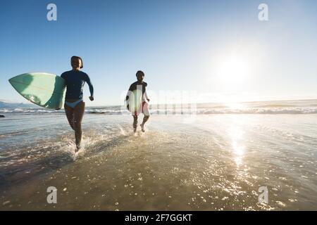 Glückliches afroamerikanisches Paar, das mit Surfbrettern aus dem Meer rennt