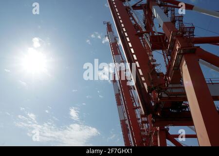 Rote Portalkrane mit weißen Streifen in vertikaler Position im Containerterminal mit blauem Himmel im Hintergrund warten auf den Frachtbetrieb in Kwangyang. Stockfoto