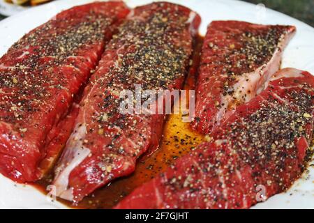 Nahaufnahme von rohen Steaks, gewürzt und auf einem weißen Teller mariniert. Stockfoto