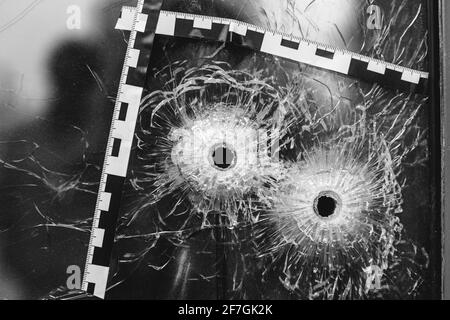 Einschusslöcher in einem Glasfenster, das mit einem gekennzeichnet ist Polizeiband Stockfoto