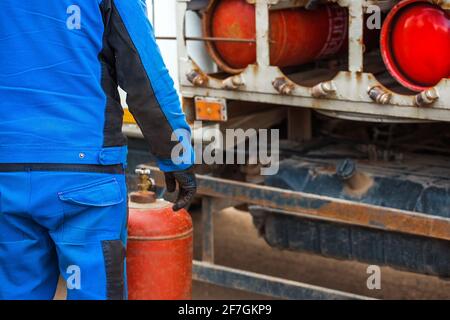 Ein männlicher Industriearbeiter steckt eine Gasflasche in eine Gasmaschine. Ausrüstung für den sicheren Transport von Propangasflaschen. Stockfoto