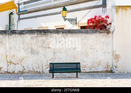 Holzbank auf dem weiß getünchten Wandhintergrund mit traditioneller portugiesischer Architektur hinter Faro, Algarve, Portugal Stockfoto