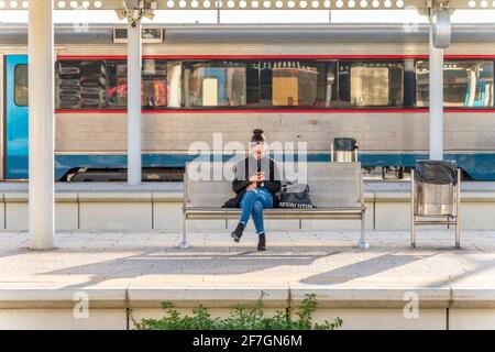 Faro, Portugal - 24. März 2021: Junge Frau mit dem Telefon auf dem Bahnsteig für den Zug Stockfoto