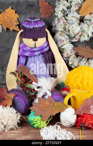 Der gestrickte lila Spielzeughase sitzt in Gewirr aus Fäden und Herbsten. Stockfoto