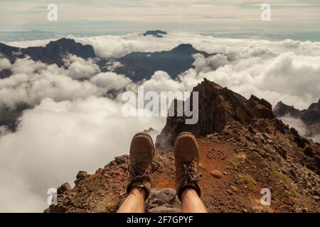Subjektive Sicht Aufnahme der Landschaft und Wanderschuhe eines Mannes, der auf der Spitze des Aussichtspunkts Roque de los Muchachos auf der Insel sitzt Stockfoto