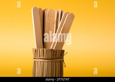Hölzerne Eisstäbchen in Bambusvase auf gelbem Hintergrund. Minimales Konzept der geschäftlichen Teamarbeit Stockfoto