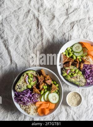 Minimalistische Food-Fotografie - zwei vegane Poke-Schüsseln mit hoisin mariniertem Tempeh, Reis und frischem, rohem Gemüse auf einem Küchentisch Stockfoto