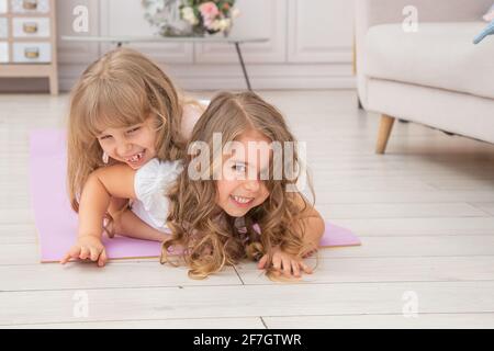 Horizontales Foto von paar kleinen Mädchen spielen auf Yoga-Matte lächeln im Wohnzimmer, gesunde Lebensgewohnheiten und Lifestyle-Konzept. Stockfoto