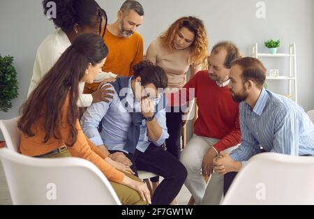 Verschiedene Menschen trösten und unterstützen den jungen Mann, der in der Gruppe weint Therapiesitzung Stockfoto