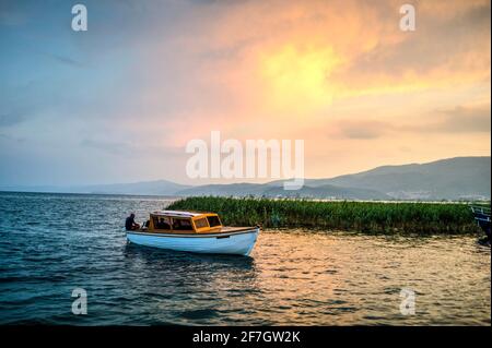 Boot im Wasser des Sees, Berge in der Ferne, dicke Wolken am Himmel. Blaue und grüne Farben mit vielen Details. Stockfoto
