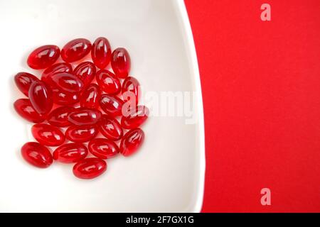 Krillöl rote Gelatine Kapseln close-up.Omega-Fettsäuren.natürliche Nahrungsergänzungsmittel und Vitamine.Rote Kapseln mit Krillöl in einer weißen Keramikschale Stockfoto