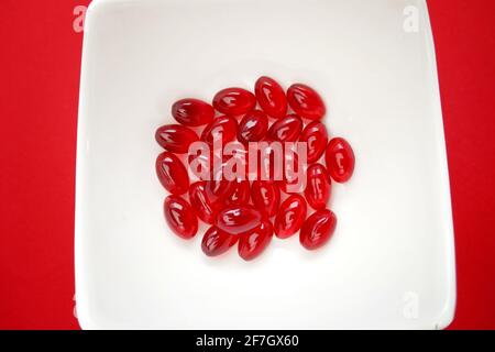 Krillöl rote Gelatine Kapseln close-up.Omega-Fettsäuren.natürliche Nahrungsergänzungsmittel und Vitamine.Rote Kapseln mit Krillöl in einer weißen Tasse auf Ein leuchtendes Rot Stockfoto