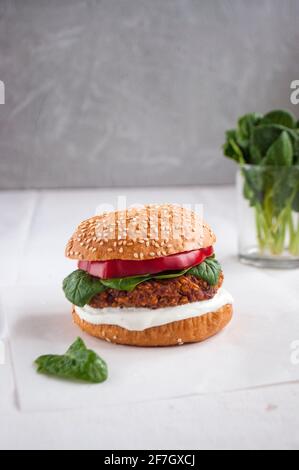 Veganer Burger mit roten Bohnen, rotem Pfeffer, Spinat, weißem Joghurt und frischen Salatblättern und geschnittenem Gemüse im Hintergrund. Stockfoto