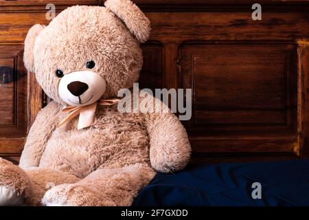 Ein riesiger beiger Teddybär mit einem Bogen schlingt gegen ein Mahagoni-Kopfteil in Toronto, Ontario, Kanada. Stockfoto