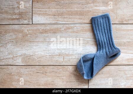 Eine einzelne gerippte halbwadenblaue Wollsocke, die ihren Partner vermisst, liegt auf einem goldbeigen Fliesenboden, der in Sonnenlicht getaucht ist, in Toronto, Ontario, Kanada. Stockfoto