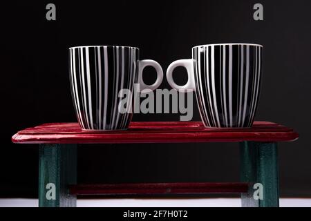 Schwarz-weiße Kaffeetassen auf Holzhintergrund vor schwarzem Hintergrund. Stockfoto