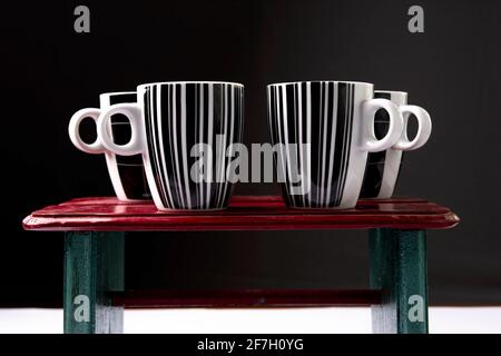Schwarz-weiße Kaffeetassen auf Holzhintergrund vor schwarzem Hintergrund. Stockfoto
