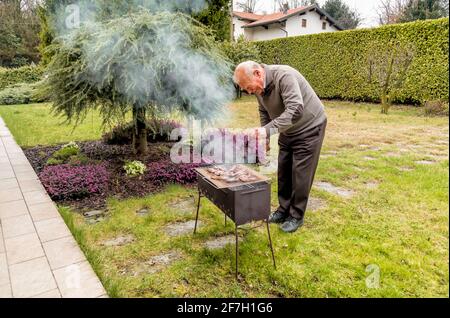 Senior man gegrillt das Fleisch auf Holzkohlegrill draußen im Garten. Stockfoto