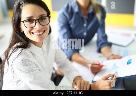 Portrait einer attraktiven Arbeiterin in stilvoller schwarzer Brille diskutieren Arbeitsmoment mit einer Kollegin Stockfoto