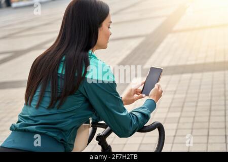 Hübsche Dame, die sich an den Lenker eines Fahrrads lehnt und Über Telefon Stockfoto