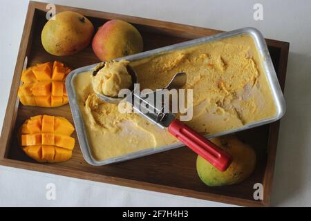 Ausschaufeln von Mango-Eis zum Servieren aus einem Tablett, das außerhalb des Gefrierschranks aufbewahrt wird. Ein Genuss in der Sommerhitze. Stockfoto