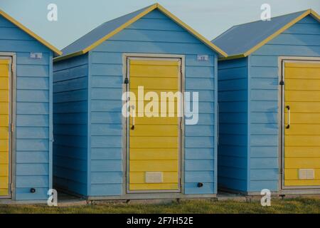 Strandhütten, blau gestrichen mit gelben Türen, gesehen an einem Strand in der Nähe von Bognor Regis, West-Sussex, Großbritannien. Stockfoto