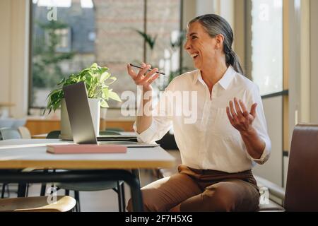 Geschäftsfrau sitzt und redet am Smartphone. Frau im Büro, die über das Lautsprechertelefon kommuniziert und lächelt. Stockfoto