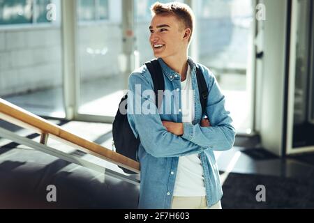 Junger Mann mit überkreuzten Armen, der wegblickt und lächelt. universitätsstudentin steht an der Treppe im College Stockfoto