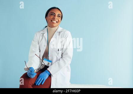 Porträt einer fröhlichen Ärztin, die wegschaut und lächelt. Medizinisches Fachpersonal mit Laborkittel und Handschuhen. Stockfoto