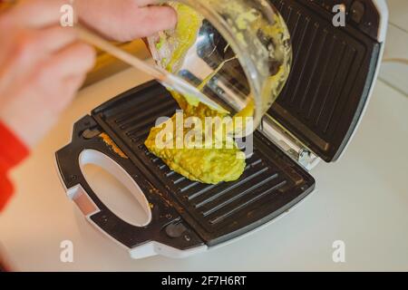 Eine Frau, die in einem Toaster ein Avocado-Omelette zubereitet oder zubereitet. Gutes, köstliches LCHF-Essen aus Avocado-Basis, geröstet in einem Grill-Toaster. F Stockfoto