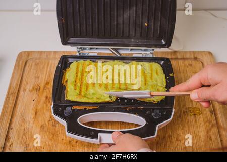 Frau, die in einem Toaster ein Avocado-Omelette zubereitet oder zubereitet. Gutes, köstliches LCHF-Essen aus Avocado-Basis, geröstet in einem Grill-Toaster. Frisch, er Stockfoto