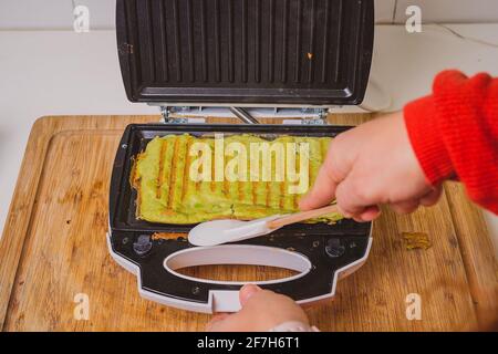 Frau, die in einem Toaster ein Avocado-Omelette zubereitet oder zubereitet. Gutes, köstliches LCHF-Essen aus Avocado-Basis, geröstet in einem Grill-Toaster. Frisch, er Stockfoto