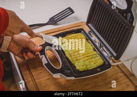 Frau, die in einem Toaster ein Avocado-Omelette zubereitet oder zubereitet. Gutes, köstliches LCHF-Essen aus Avocado-Basis, geröstet in einem Grill-Toaster. Frisch, er Stockfoto