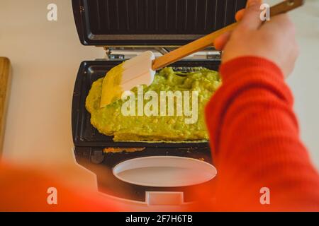 Eine Frau, die in einem Toaster ein Avocado-Omelette zubereitet oder zubereitet. Gutes, köstliches LCHF-Essen aus Avocado-Basis, geröstet in einem Grill-Toaster. F Stockfoto