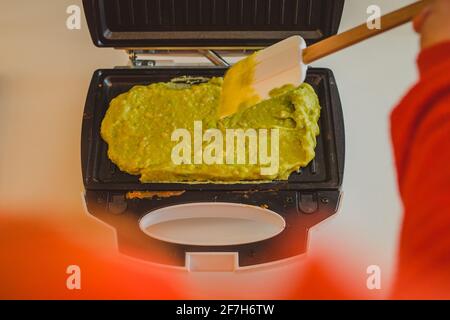 Eine Frau, die in einem Toaster ein Avocado-Omelette zubereitet oder zubereitet. Gutes, köstliches LCHF-Essen aus Avocado-Basis, geröstet in einem Grill-Toaster. F Stockfoto