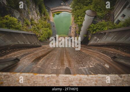 Gruselige Aussicht vom kleinen, aber steilen Staudamm für das Wasserkraftwerk in Moste, Slowenien. Blick auf den hidroelektrischen Damm von oben, direkt nach unten. Stockfoto