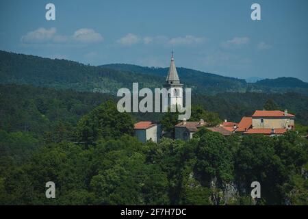 Dorf Skocjan, mit einem sichtbaren Glockenturm der St. Kancijan Kirche, der sich an einem Sommertag weit über der Schlucht der Skocjan Höhlen erhebt. Stockfoto